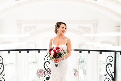 Girl in a wedding dress standing in front of a banister holding a bouquet of different colored roses.